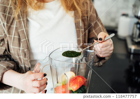Close up woman adding spirulina or chlorella powder during making smoothie on the kitchen. Superfood supplement. Healthy detox vegan diet. Healthy dieting eating, weight loss program. Selective focus Close up woman adding spirulina or chlorella powder during making smoothie on the kitchen. Superfood supplement. Healthy detox vegan diet. Healthy dieting eating, weight loss program. Selective focus 118477757