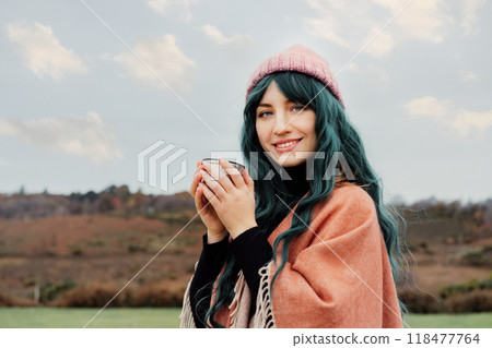Portrait of smiling Woman in hat wrapped in Shawl Poncho drinking hot drink from thermos cup enjoying autumn landscape view. Feeling harmony, relax, personal fulfilment. Local travel lifestyle 118477764