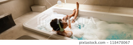 A woman is bathing in a tub of bubbles in the bathroom A woman is bathing in a tub of bubbles in the bathroom 118478067