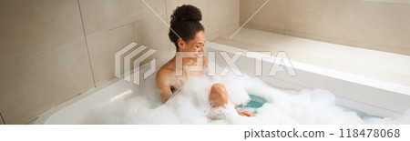 Woman enjoying a foamfilled bath in a bathtub, relaxing in the bathroom Woman enjoying a foamfilled bath in a bathtub, relaxing in the bathroom 118478068