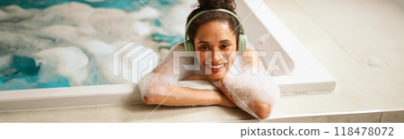 a woman wearing headphones is taking a bath in a hot tub a woman wearing headphones is taking a bath in a hot tub 118478072