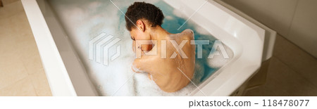 A woman leisurely bathes in a foamy bathtub, barechested and relaxed 118478077