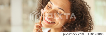 a woman is smiling while using a facial roller on her face 118478088