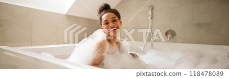 A happy woman is bathing in a foamfilled bathtub, smiling at the fixture 118478089