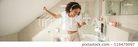 A woman with headphones dances in a bathroom, brushing her teeth A woman with headphones dances in a bathroom, brushing her teeth 118478097