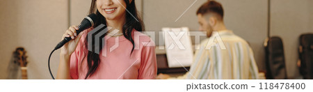 Young Woman Singing into Microphone in Music Studio Young Woman Singing into Microphone in Music Studio 118478400