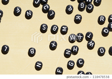 Scattered black alphabet letters on beige surface with randomized flat layout 118478538