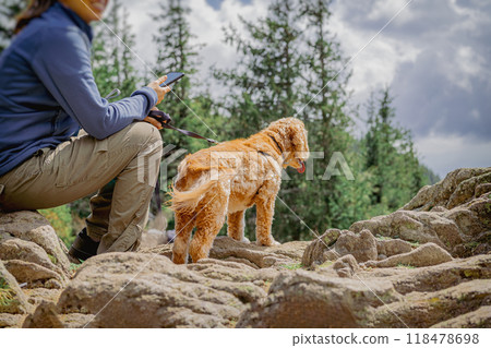 Abstract person sitting on rocky terrain with golden retriever on leash, enjoying nature hike 118478698