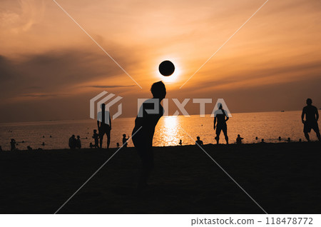 Silhouettes of Asian men playing beach football on beach by sea at sunset 118478772