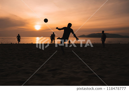 Silhouettes of a group of Asian men playing traditional beach football on beach by the sea at sunset 118478777