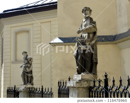 Stone figure of a man against the background of an old wall on a column of an iron fence 118478960