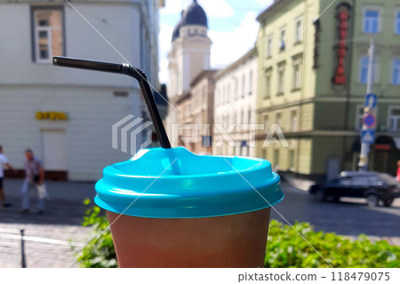 Refreshing Coffee in a Brown Cup With Blue Lid Against a City Summer Backdrop Refreshing Coffee in a Brown Cup With Blue Lid Against a City Summer Backdrop 118479075