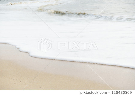 gentle waves lap against sandy shore, creating serene and calming atmosphere. soft foam contrasts beautifully with golden sand, inviting relaxation and tranquility 118480569