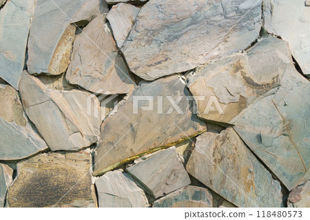 Natural stone wall texture features irregularly shaped slate pieces in earthy tones. unique patterns and colors create rustic and organic feel, perfect for various design applications 118480573