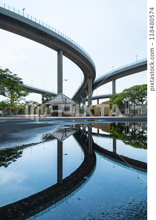 A serene urban scene featuring small building reflected in puddle, surrounded by modern overpasses. contrast between nature and infrastructure creates unique visual experience 118480574