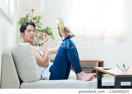 Young man putting on make-up in the living room Young man putting on make-up in the living room 118480824