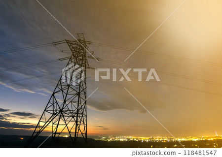 Transmission and long distance distribution of electricity concept. High voltage tower with electric power lines stretching on dark blue starry sky.and bright distant city lights background. 118481547