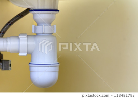 Detail view of new modern ceramic white washbasin sink connection to sewer on copy space background of light beige ceramic tiles. Professional plumbing and installation concept. Detail view of new modern ceramic white washbasin sink connection to sewer on copy space background of light beige ceramic tiles. Professional plumbing and installation concept. 118481792