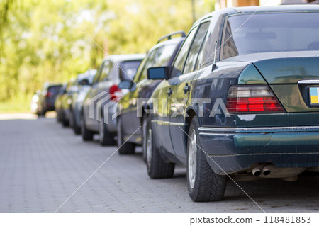 Long row of cars parked in quiet neighborhood on clean empty paved street on background of beautiful green trees on bright sunny summer or spring day. 118481853