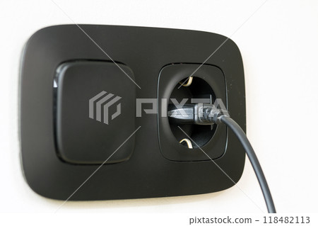 Black power cord cable plugged into european wall outlet on white plaster wall 118482113