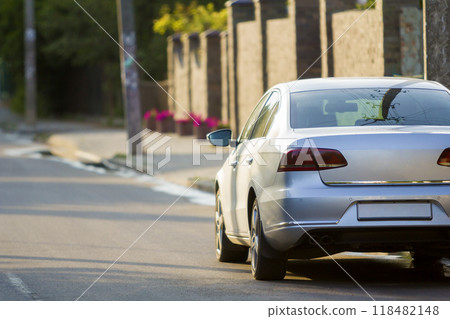 Close-up back view of new shiny expensive silver car moving along city street on blurred trees, cars and buildings background on sunny summer day. Comfortable transportation and speed in modern life. Close-up back view of new shiny expensive silver car moving along city street on blurred trees, cars and buildings background on sunny summer day. Comfortable transportation and speed in modern life. 118482148
