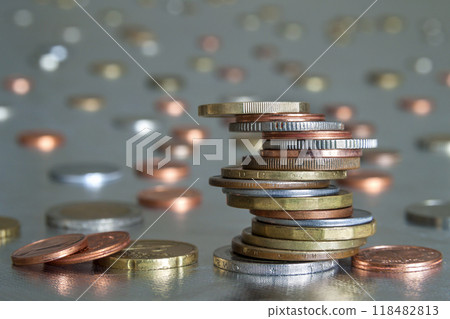 Pile of shiny coins different sizes and colors stacked unevenly on each other on colorful blurred blue abstract background. Money saving and financial risk concept. 118482813
