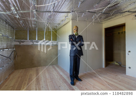 Strange man in businessman suit and gas protection mask inside a room under renovation works. Strange man in businessman suit and gas protection mask inside a room under renovation works. 118482898