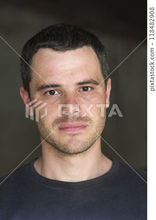 Portrait of young handsome black-haired unshaven confident successful man in casual T-shirt with white teeth and shiny black eyes looking in camera on dark background. 118482908