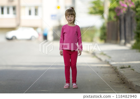 Full length portrait of cute small girl in pink casual clothing and long blond pony tail looking in camera standing on blurred bright sunny street background. Beauty of childhood concept. 118482940