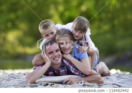 Family portrait of young happy mother, father and two cute blond children, boy and girl on bright summer day with green bokeh background. Happy family relations, love, care and perfect holiday concept 118482942