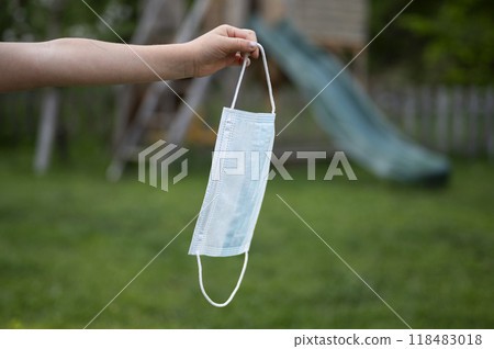 Hand of a child holding a medical protective mask over green natures background Hand of a child holding a medical protective mask over green natures background 118483018