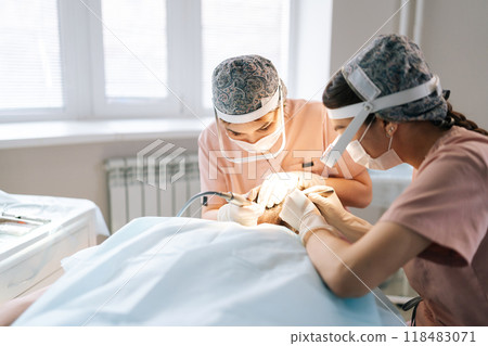 Professional two female trichologist collecting hair follicles from back of head of male patient for hair transplantation in clinic. Process of hair transplant with FUE Sapphire method. Professional two female trichologist collecting hair follicles from back of head of male patient for hair transplantation in clinic. Process of hair transplant with FUE Sapphire method. 118483071