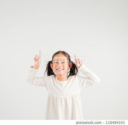 Asian happy portrait cute young kid girl makes gesture fingers point upwards above presenting product something, studio shot isolated on white background, kindergarten children woman smile 118484101