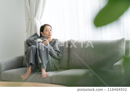 Woman sitting on sofa and using smartphone Woman sitting on sofa and using smartphone 118484932