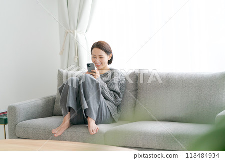 Woman sitting on sofa and using smartphone Woman sitting on sofa and using smartphone 118484934