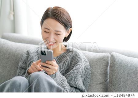 Woman sitting on sofa and using smartphone 118484974