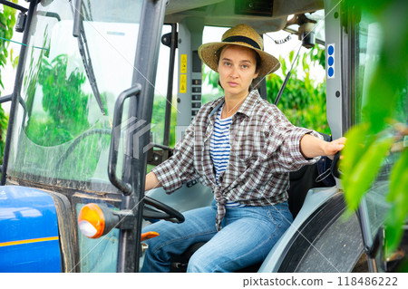 Concentrated female farmer is sitting at the wheel of a tractor 118486222