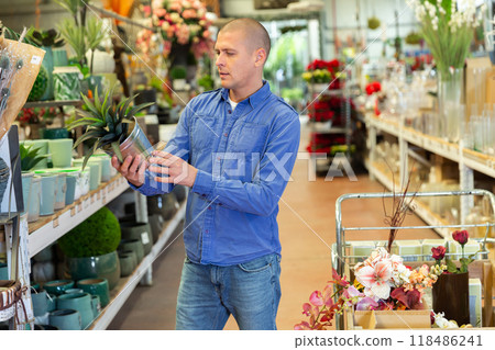 Male customer in winter clothes chooses cactus flower in shop 118486241