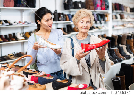 Seller helping elder woman to choose shoes 118486385