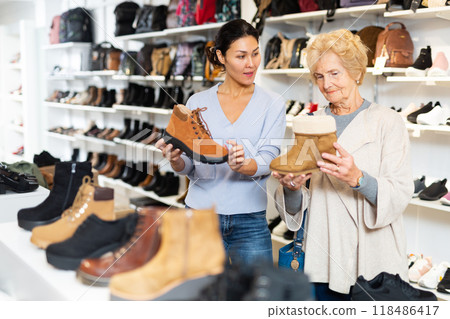 Female sales consultant helps a mature woman to choose winter shoes 118486417