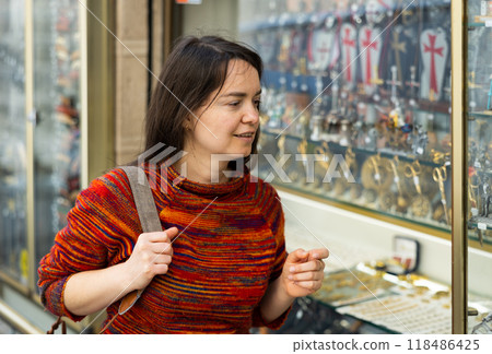 Woman tourist, standing near the window of a souvenir shop, examines the goods Woman tourist, standing near the window of a souvenir shop, examines the goods 118486425