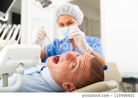 Qualified woman dentist in a protective mask treats a man patient 118486681