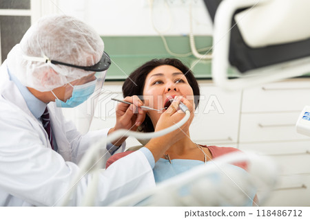 Qualified man dentist in a protective mask treats a woman patient 118486712