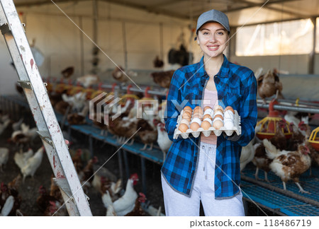 Smiling woman standing in henhouse with cardboard tray of eggs Smiling woman standing in henhouse with cardboard tray of eggs 118486719