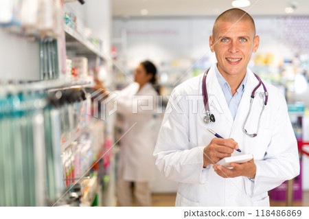 Positive pharmacist makes notes on a notebook in the sales area of pharmacy 118486869