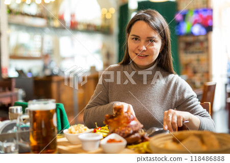 Smiling woman enjoying baked pork knuckle in restaurant 118486888