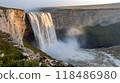 Powerful waterfall cascading down a rugged rocky cliff surrounded by thick mist and lush green foliage in a picturesque natural landscape 118486980