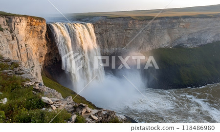 Powerful waterfall cascading down a rugged rocky cliff surrounded by thick mist and lush green foliage in a picturesque natural landscape 118486980