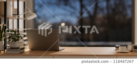 A rear view of a laptop on a wooden table, with a window showing an outdoor view at dusk. 118487267