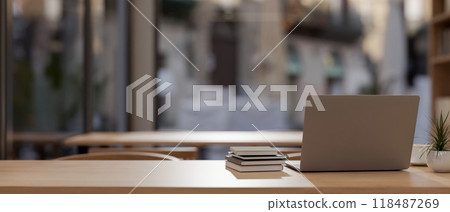 A rear view of a laptop and books on a wooden tabletop in a contemporary coffee shop. 118487269